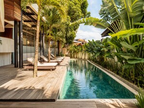A swimming pool with lounge chairs, surrounded by tropical plants and a wooden deck. - Elegant 1BR Loft with Art Deco Flair, Shared pool (Kecamatan Mengwi)