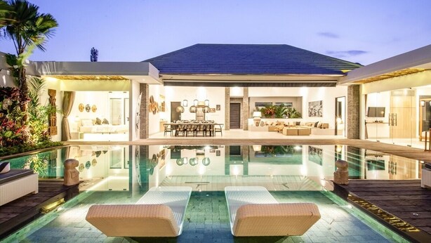 A modern house with a large swimming pool, a dining area, and a living room with a sofa and a TV.