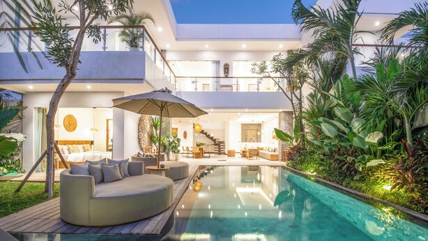 Una casa moderna con piscina, mobiliario exterior y exuberante vegetación.