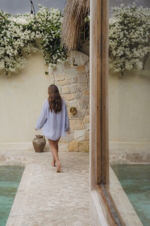 A woman walking towards a stone wall with a thatched roof and white flowers. - Serene 3BR Villa, Stylish Interiors, beach close (Uluwatu)