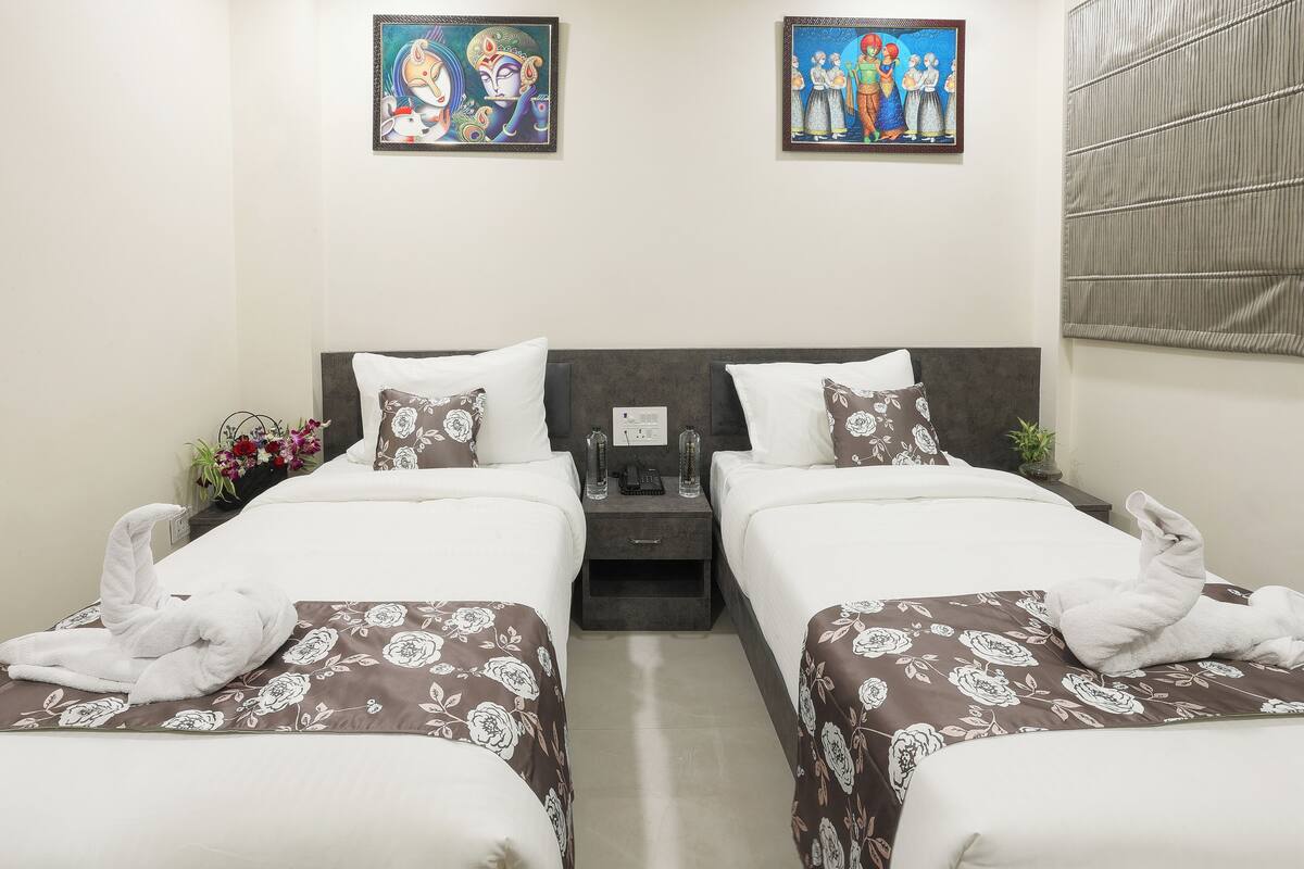A hotel room with two beds, each with a floral-patterned bedspread, a nightstand with a phone and a lamp, and artwork on the walls.