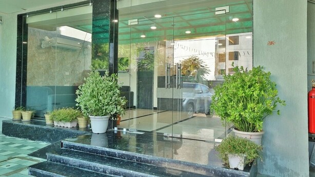 L’entrée d’un hôtel, avec une porte en verre, des plantes en pot et une voiture garée à l’extérieur.