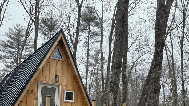 A wooden cabin with a porch, a door, and a green chair. - Sister A-Frame in Woods B (Oakland)