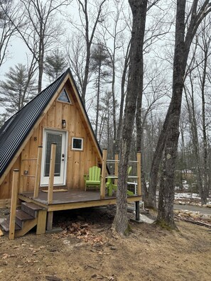 A wooden cabin with a porch, a door, and a green chair. - Sister A-Frame in Woods B (Oakland)