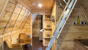 A cozy attic bedroom with a sloped ceiling, wooden walls, a loft bed, a small desk, and a staircase. - Sister A-Frame in Woods B (Oakland)