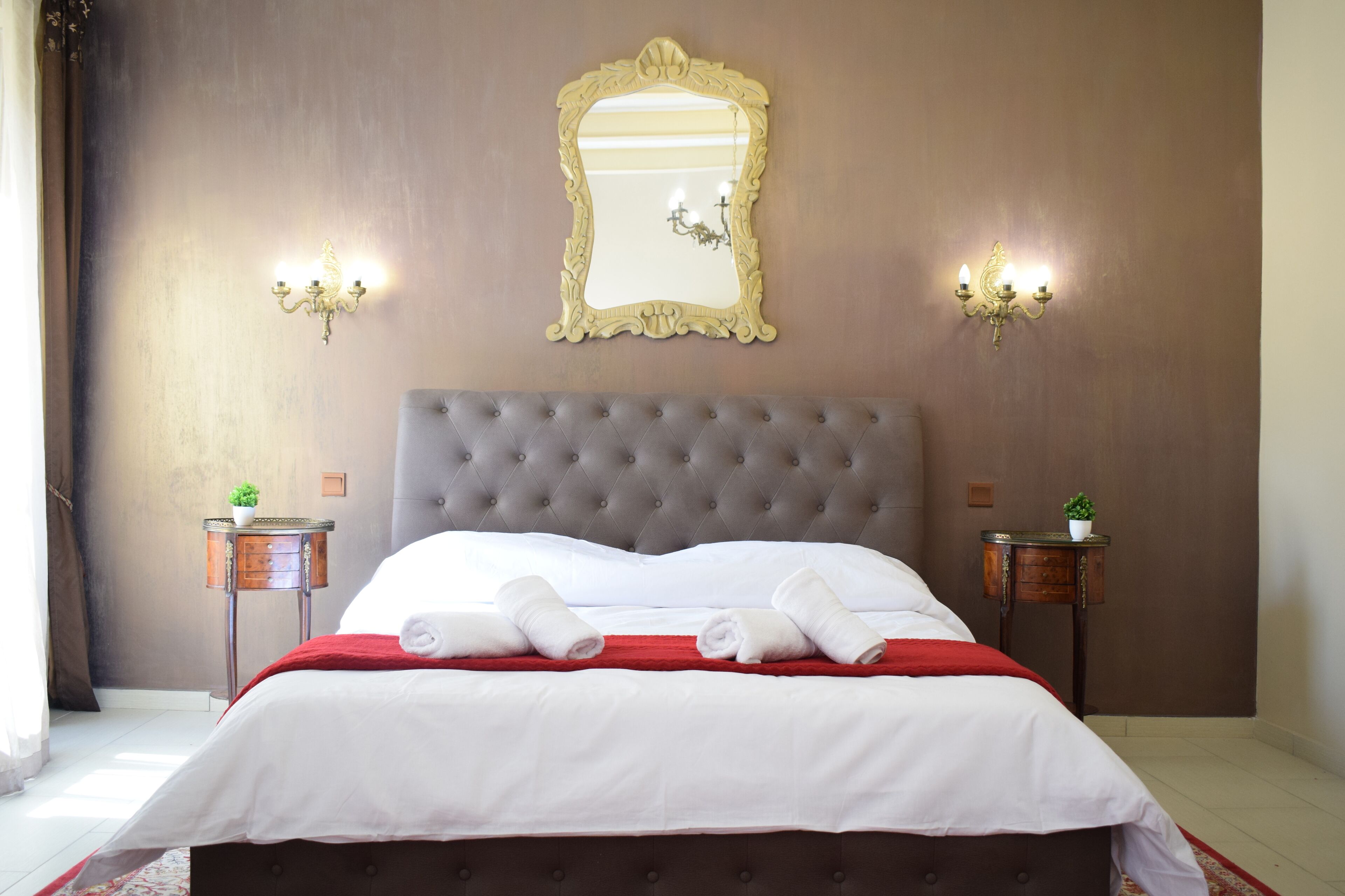 Une chambre d’hôtel avec une tête de lit capitonnée, un grand miroir, deux tables de chevet avec des lampes et des serviettes soigneusement pliées sur le lit.