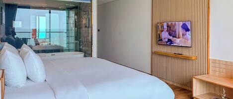 A modern hotel room with a large bed, a TV mounted on the wall, and a view of the city through a glass door.