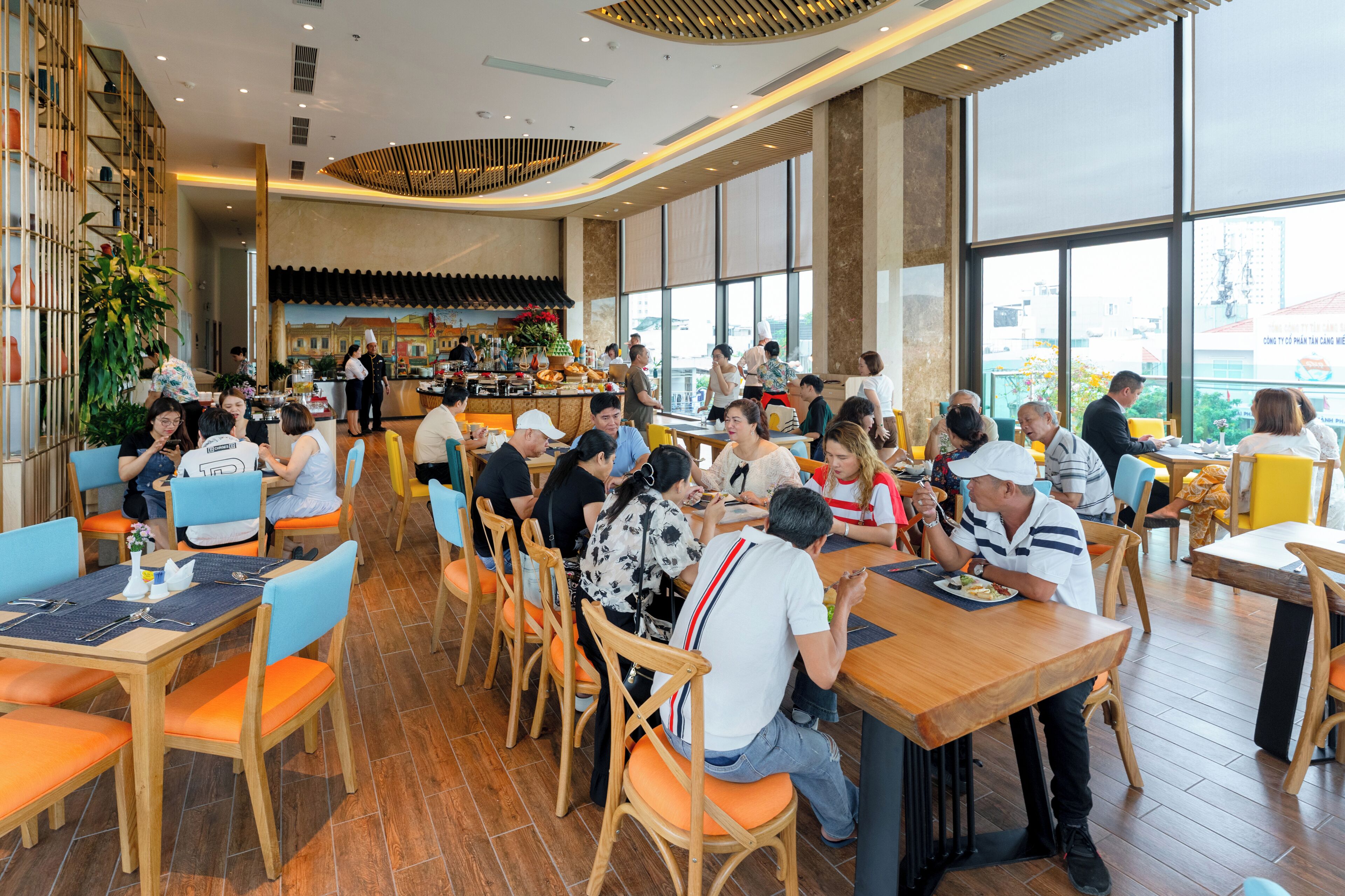 A busy restaurant with wooden tables and chairs, a bar area, and large windows.