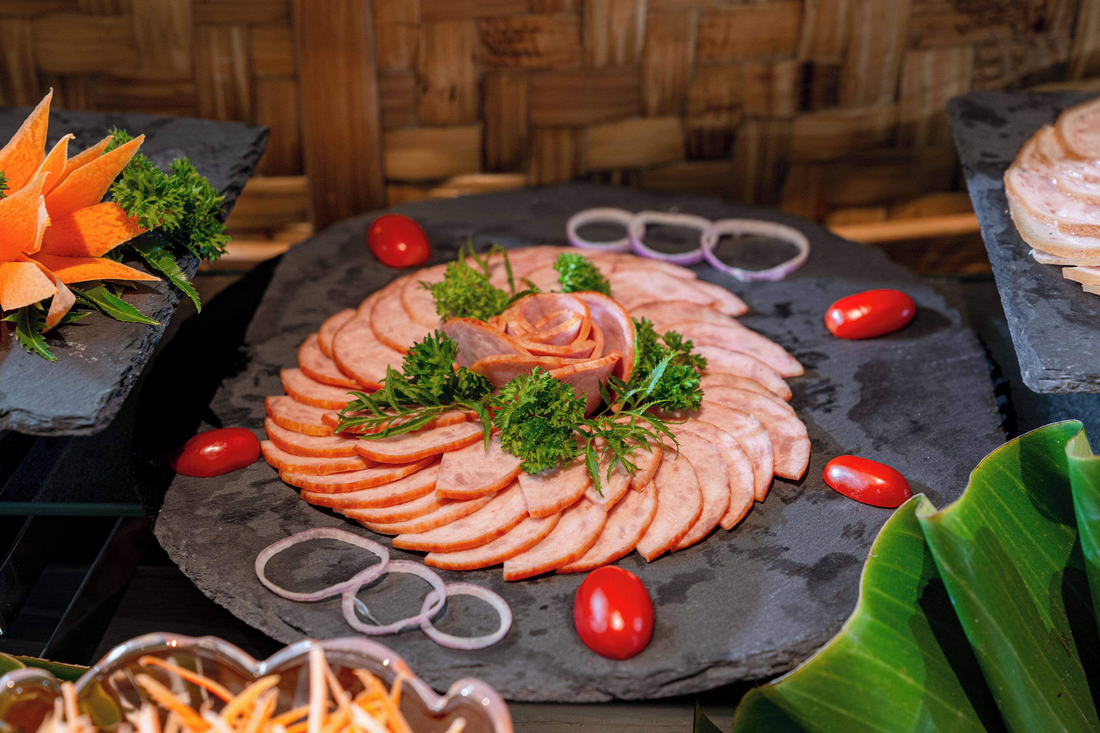 A platter of sliced meats garnished with parsley and surrounded by tomatoes and onions.
