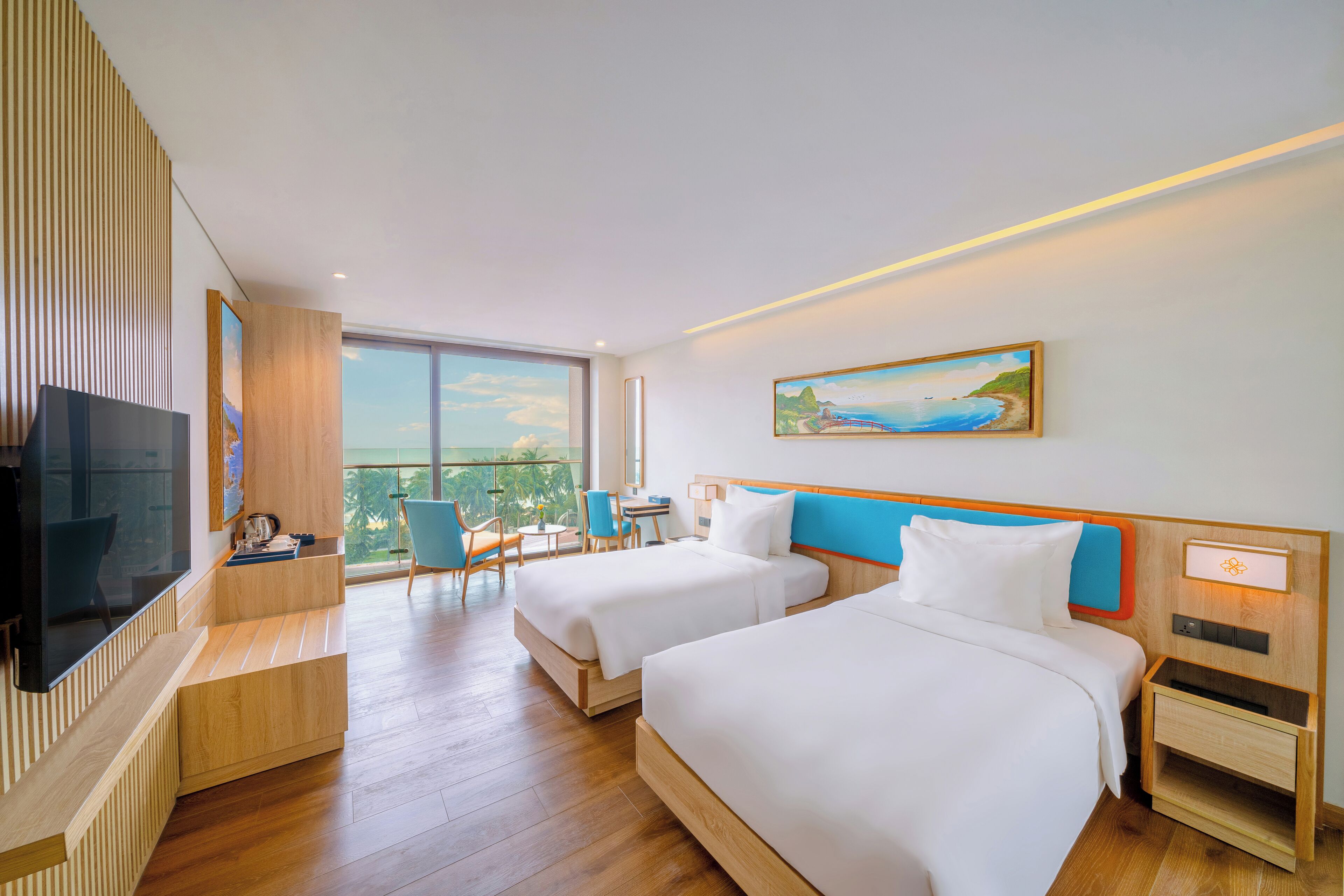 Habitación de hotel con dos camas, televisión, escritorio y balcón con vistas.