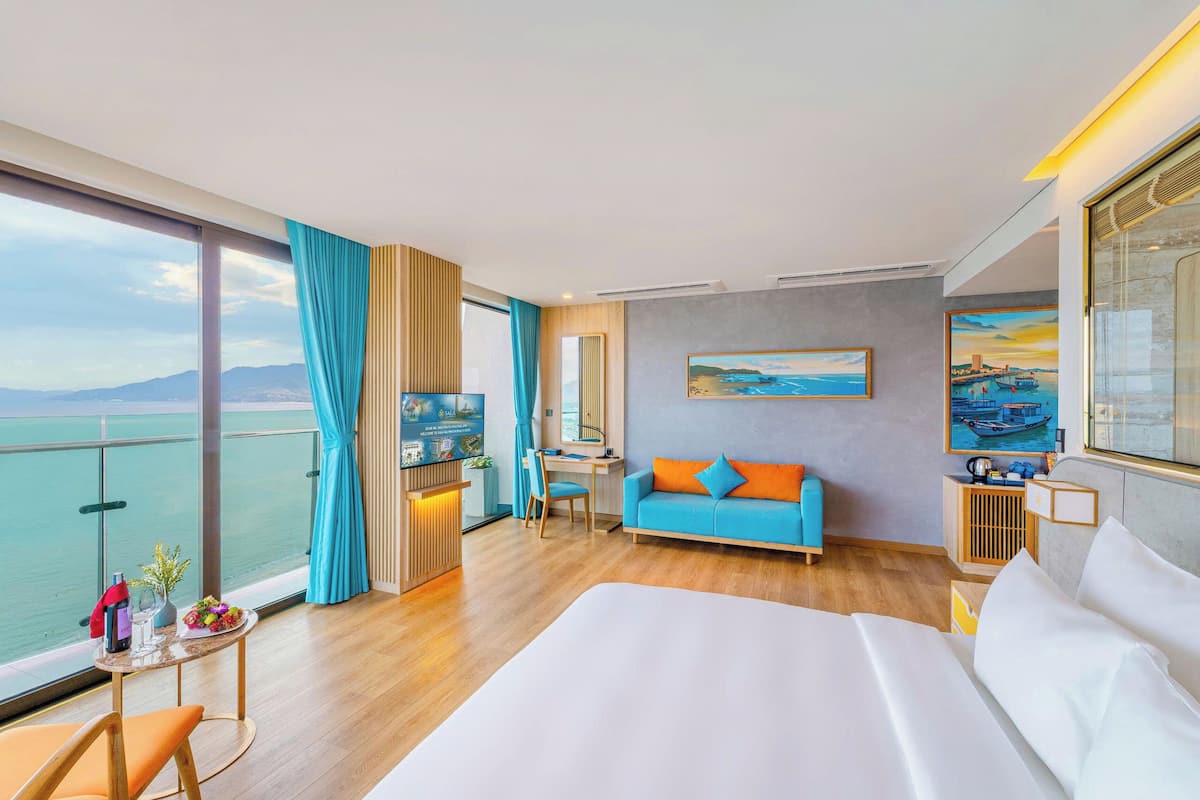 A hotel room with a large bed, a sofa, a desk, and a view of the sea.