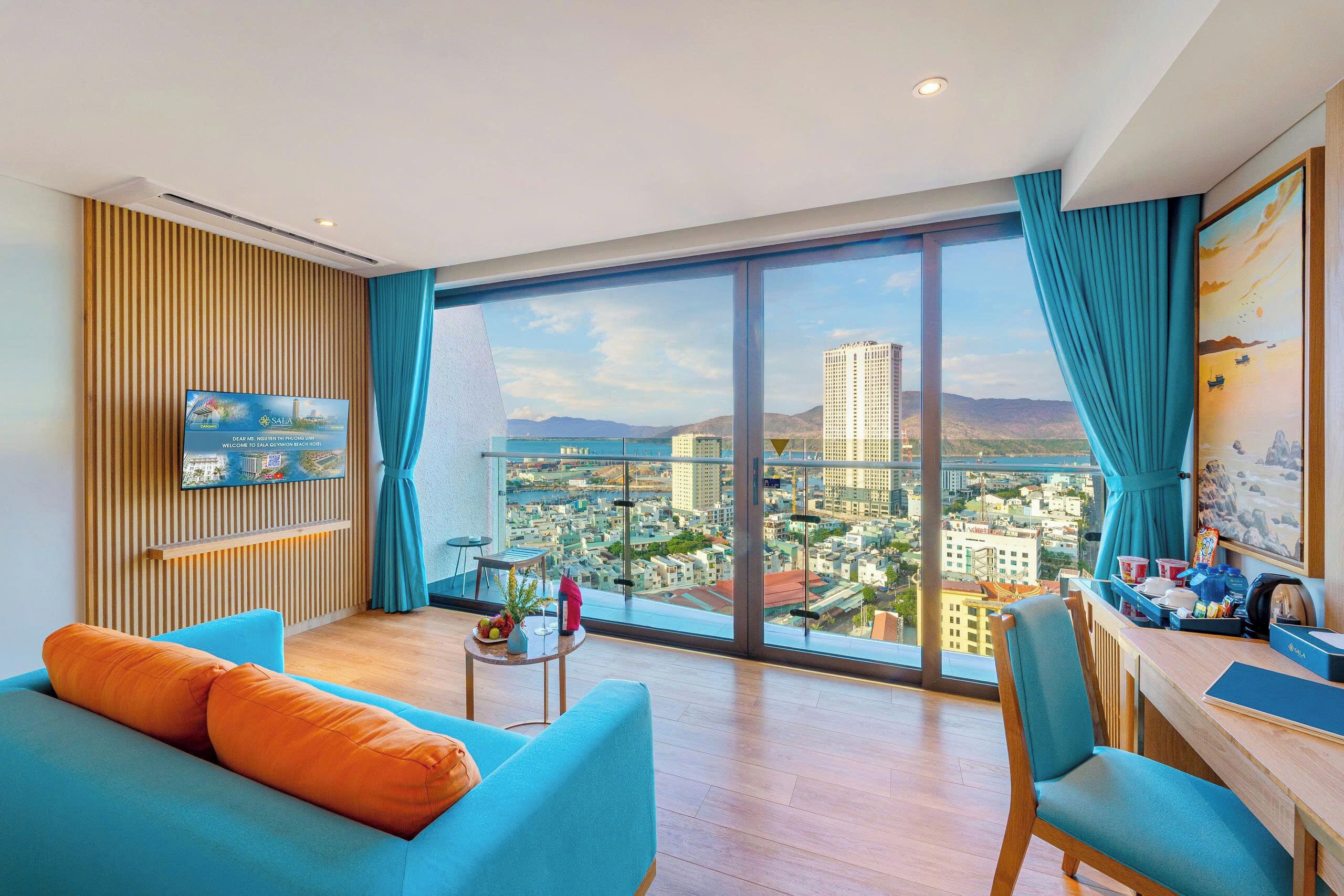 A modern living room with a large window, a flat-screen TV, a sofa, a dining area, and a view of a cityscape.