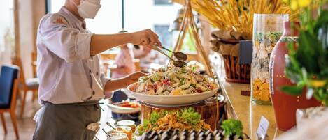 A buffet setup with various dishes and a person serving food.