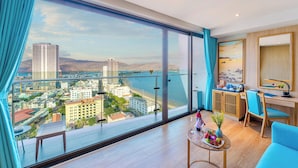 Een moderne hotelkamer met een groot balkon, een bureau en uitzicht op de stad en het water.