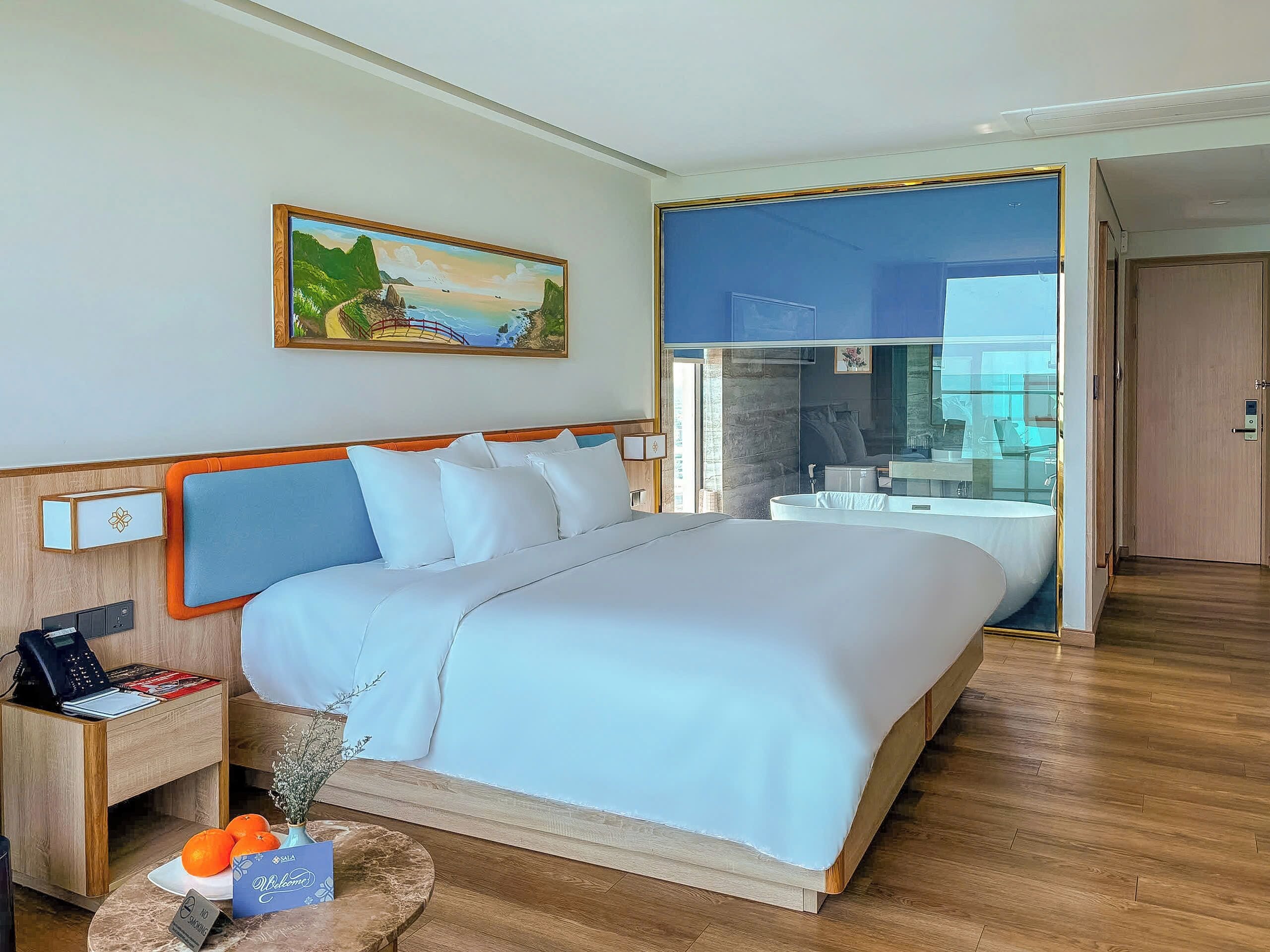 A hotel room with a bed, a nightstand, a vase with flowers, and a painting on the wall.