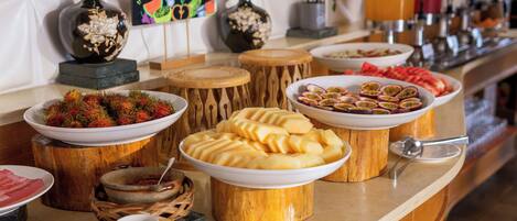 A buffet with various dishes, including fruits and pastries, arranged on a wooden stand.