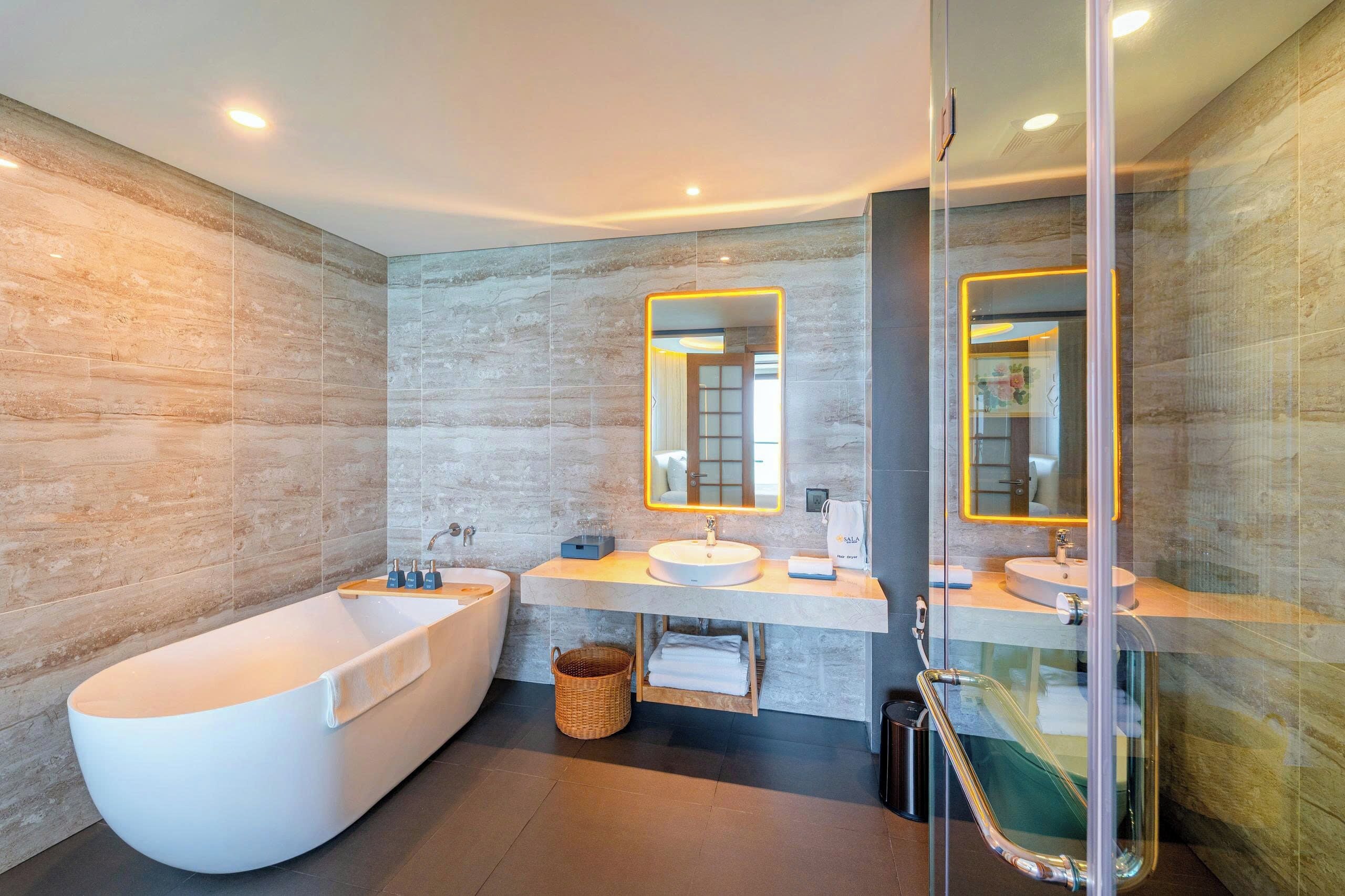 A modern bathroom with a freestanding bathtub, two sinks, and large mirrors.