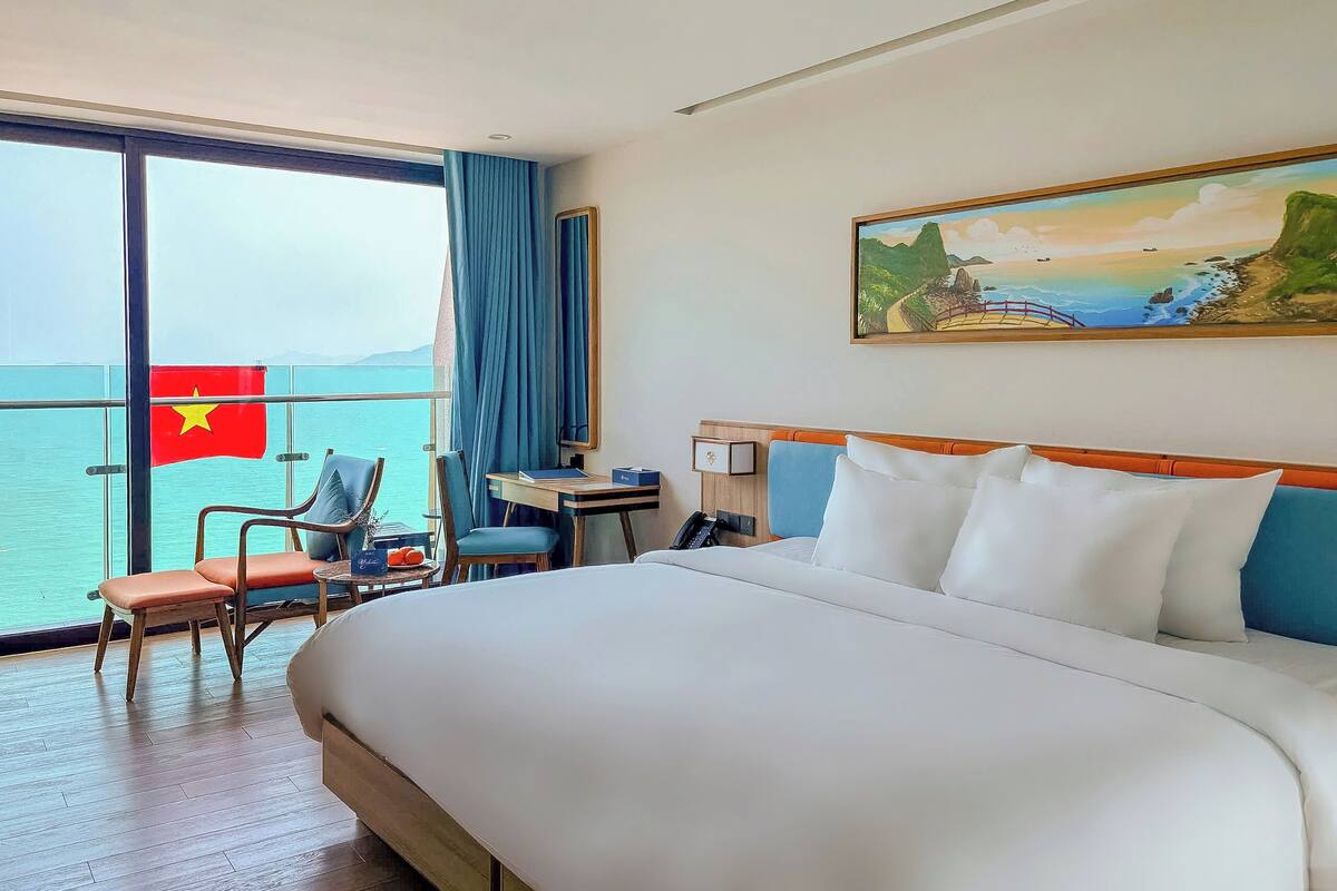 A hotel room with a bed, a desk, a chair, a phone, and a large window with a flag.