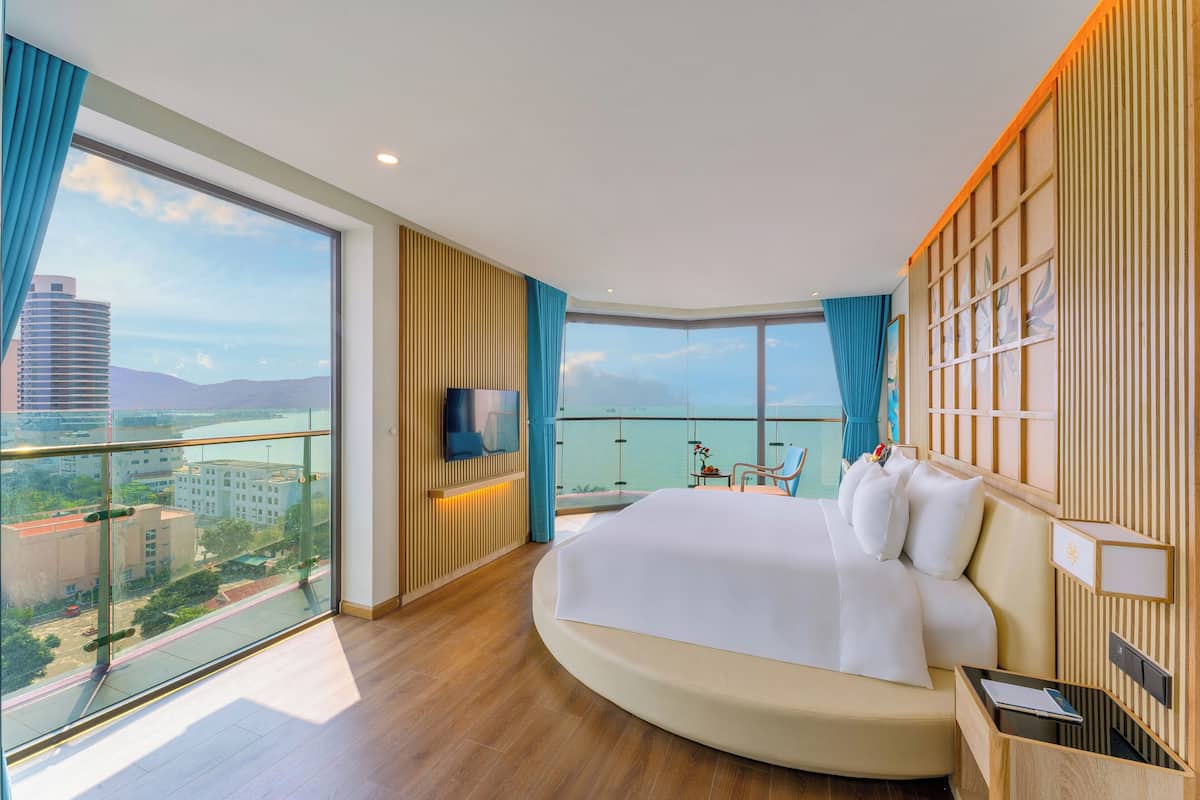 A modern hotel room with a curved bed, large windows, and a city view.