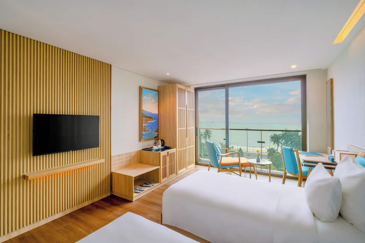 A modern hotel room with a large window, a flat-screen TV, a wooden slatted wall, a desk with a chair, and a bed.