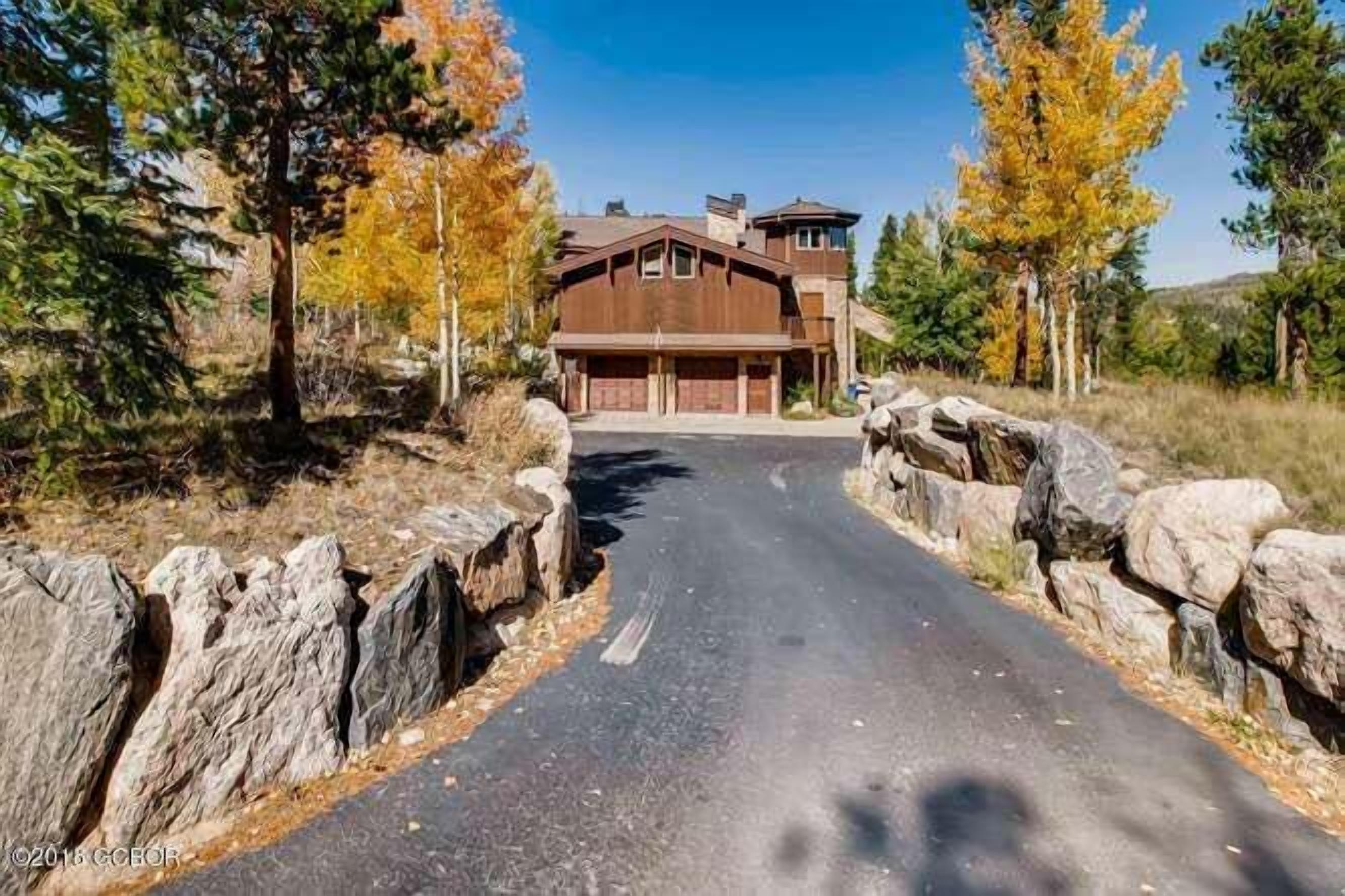 A modern house with a garage, surrounded by a stone wall and trees.