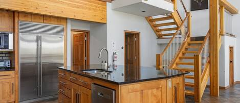 A modern kitchen with a stainless steel refrigerator, wooden cabinets, and a large island with a sink.