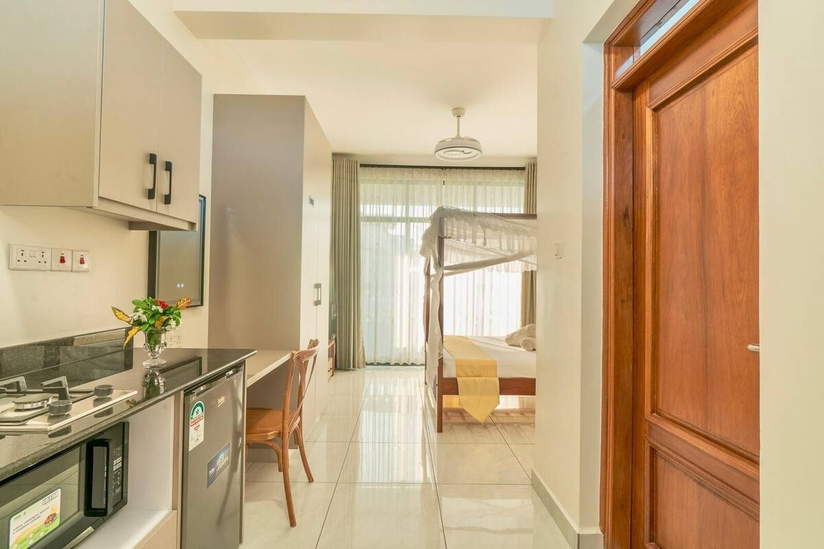 Una cocina moderna con estufa integrada, un área de comedor con mesa y sillas, una cama litera con dosel y una puerta de madera.