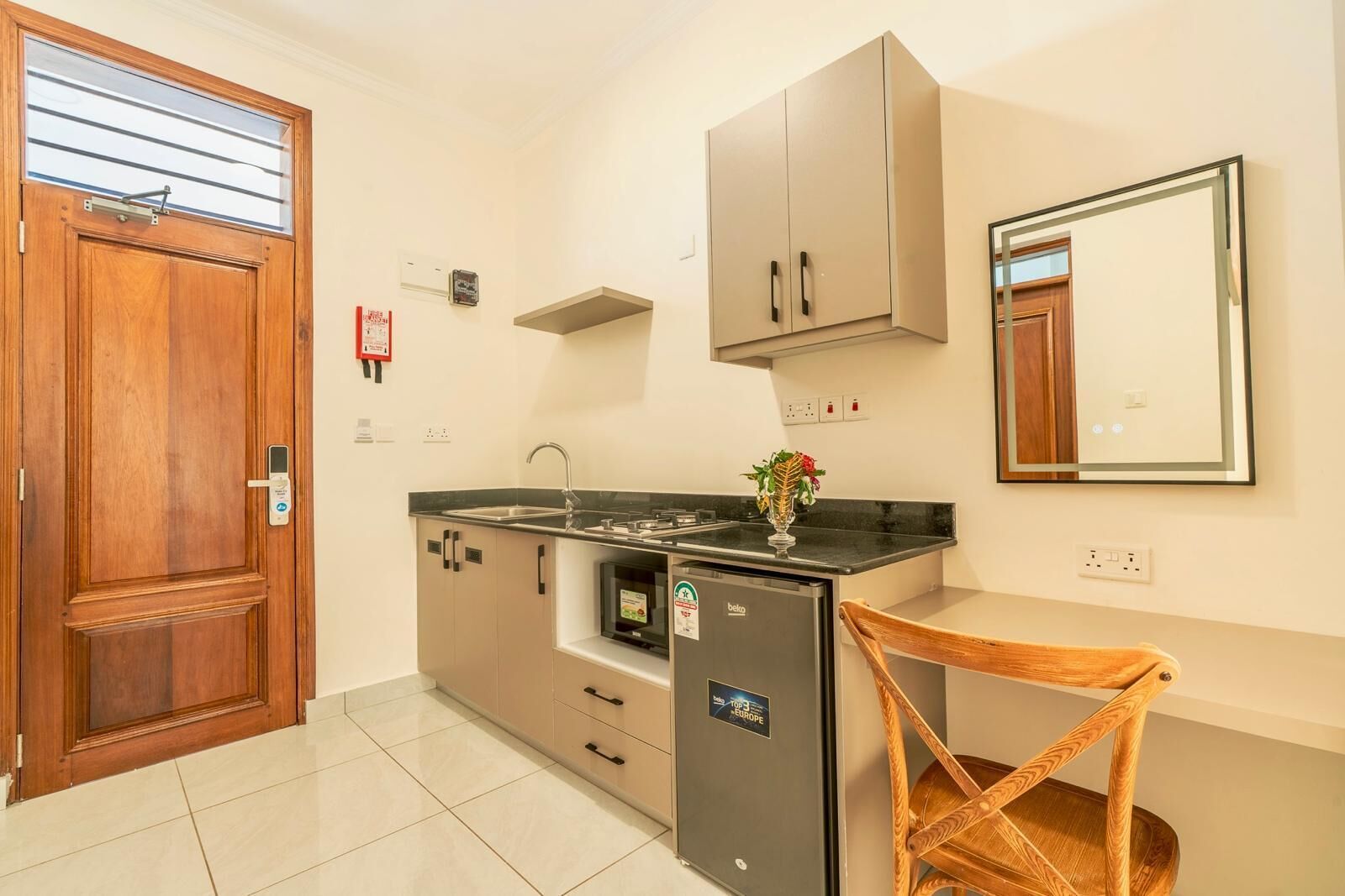 A compact kitchen with a wooden door, a built-in fridge, a sink, and a mirror above the counter.