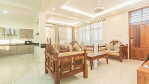 A spacious living area with a wooden sofa set, a coffee table, and a kitchen in the background. - Leshan Luxury Villas  (Diani Beach)