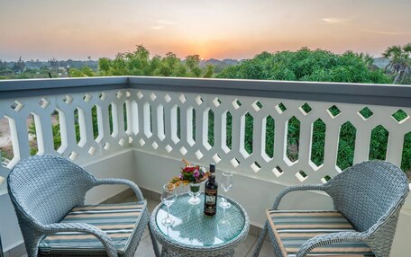 A balcony with wicker chairs and a small round table, a bottle, and a glass of wine.