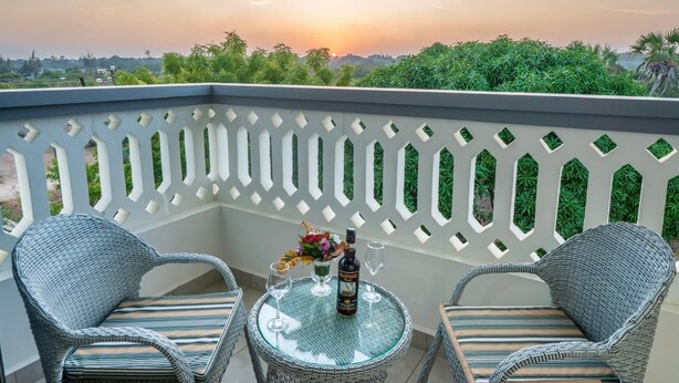 A balcony with wicker chairs and a small round table, a bottle, and a glass of wine. - Leshan Luxury Villas  (Diani Beach)