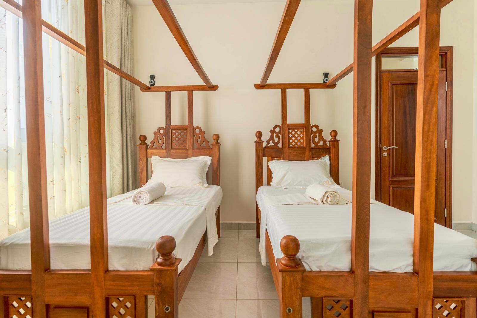 A room with two wooden four-poster beds, white linens, and a wooden door.