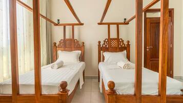 A room with two wooden four-poster beds, white linens, and a wooden door.