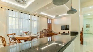 A modern kitchen with a central island, dining area with wooden chairs, and a TV mounted on the wall. - Leshan Luxury Villas  (Diani Beach)