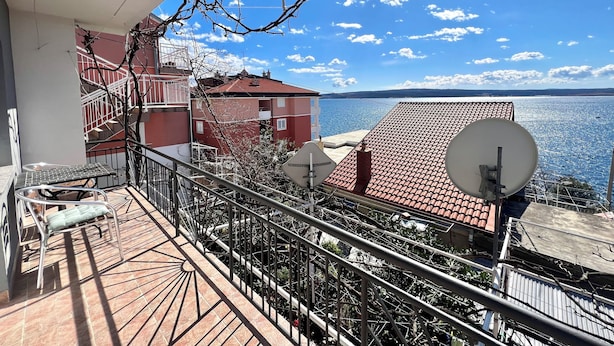 A balcony with a view of a body of water, a red building, and a satellite dish. - Apartman Mare 3 (Dramalj)