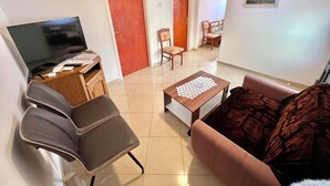 A living room with a TV, a sofa, a coffee table, and a dining area with chairs. - Apartman Mare 3 (Dramalj)