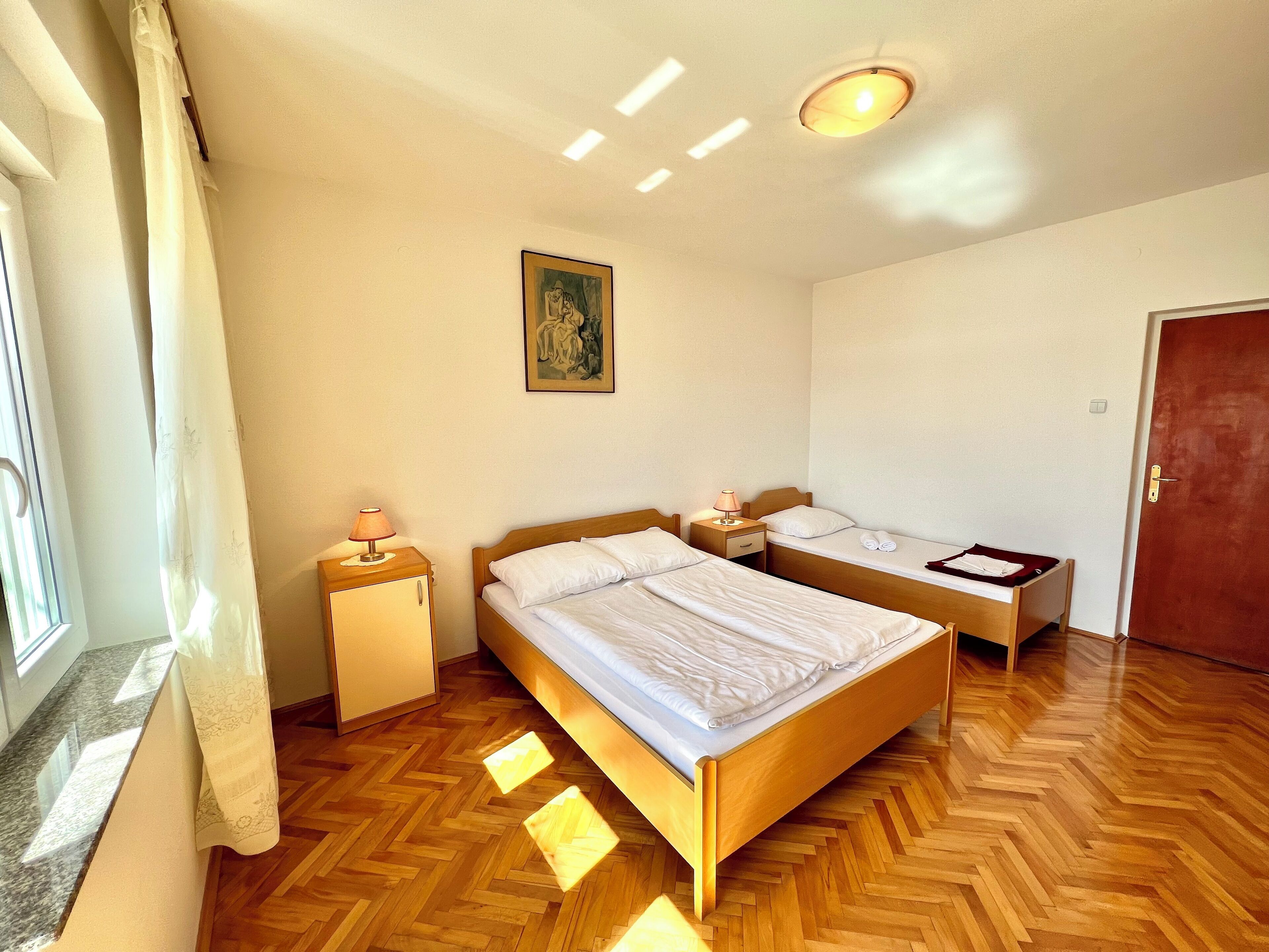 Un dormitorio con dos camas individuales, suelo de madera, un cuadro en la pared y una ventana con cortinas.