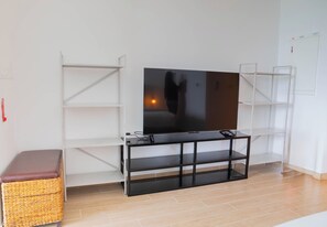 A room with a flat-screen TV on a black stand, white shelving units, and a wicker basket.