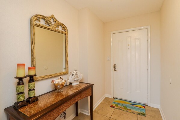 A hallway with a wooden console table, a mirror, candles, a decorative bowl, and a door with a beach-themed mat.
