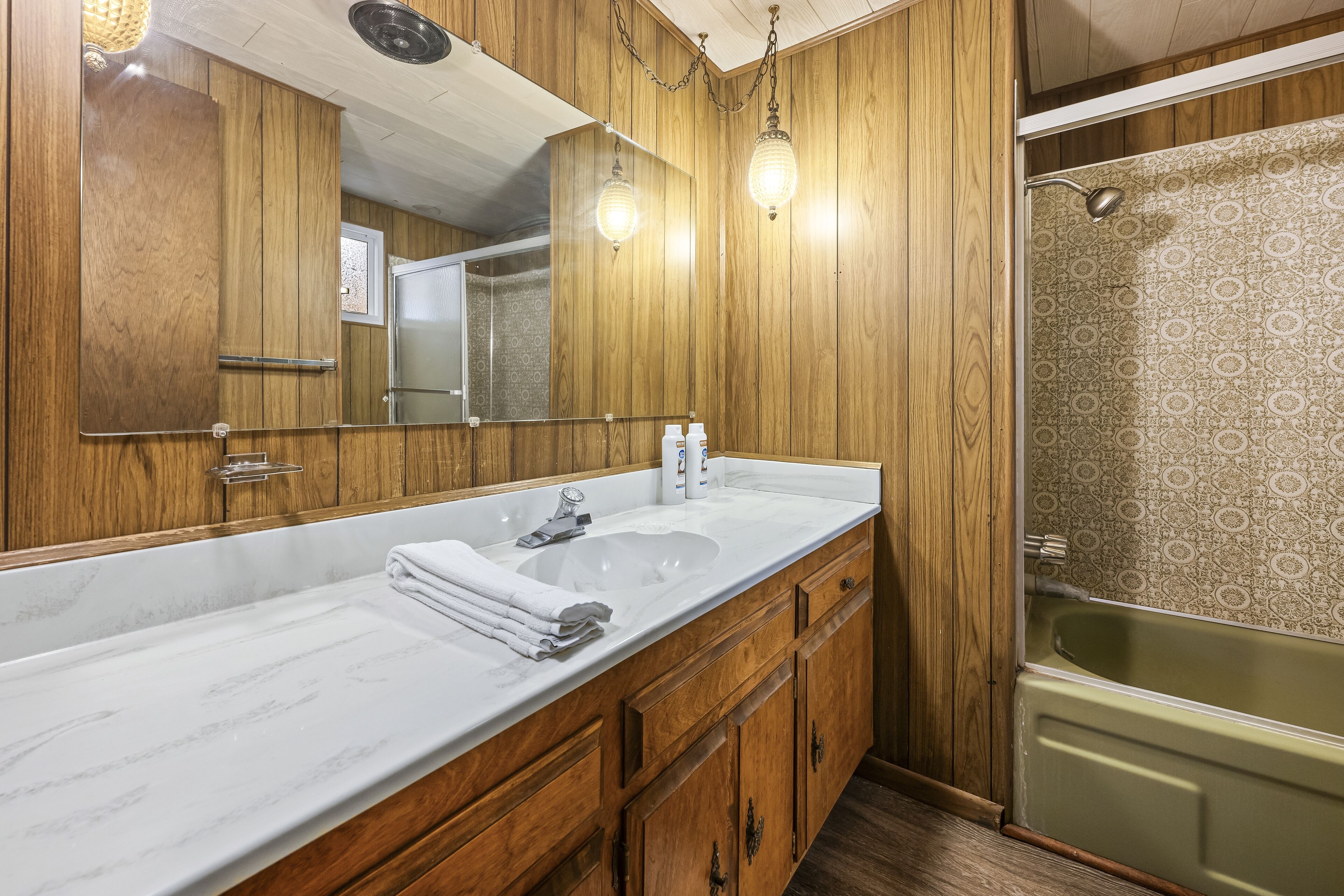 Un baño con paneles de madera, un espejo grande, un lavamanos blanco y una bañera verde.