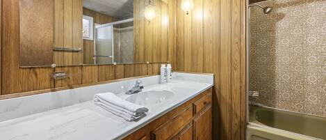 Un baño con paneles de madera, un espejo grande, un lavamanos blanco y una bañera verde.
