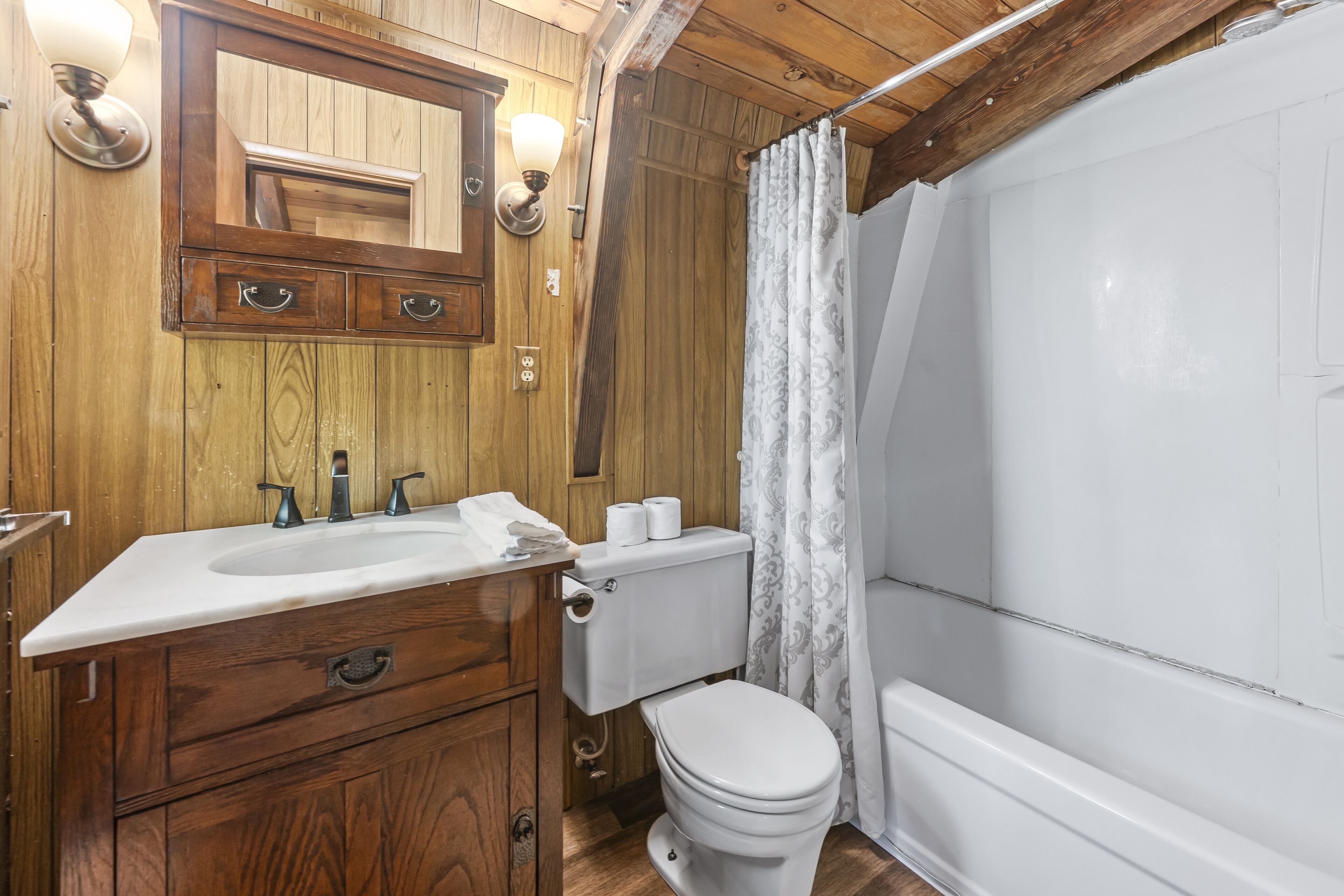 Un baño de madera con lavamanos, inodoro y bañera.
