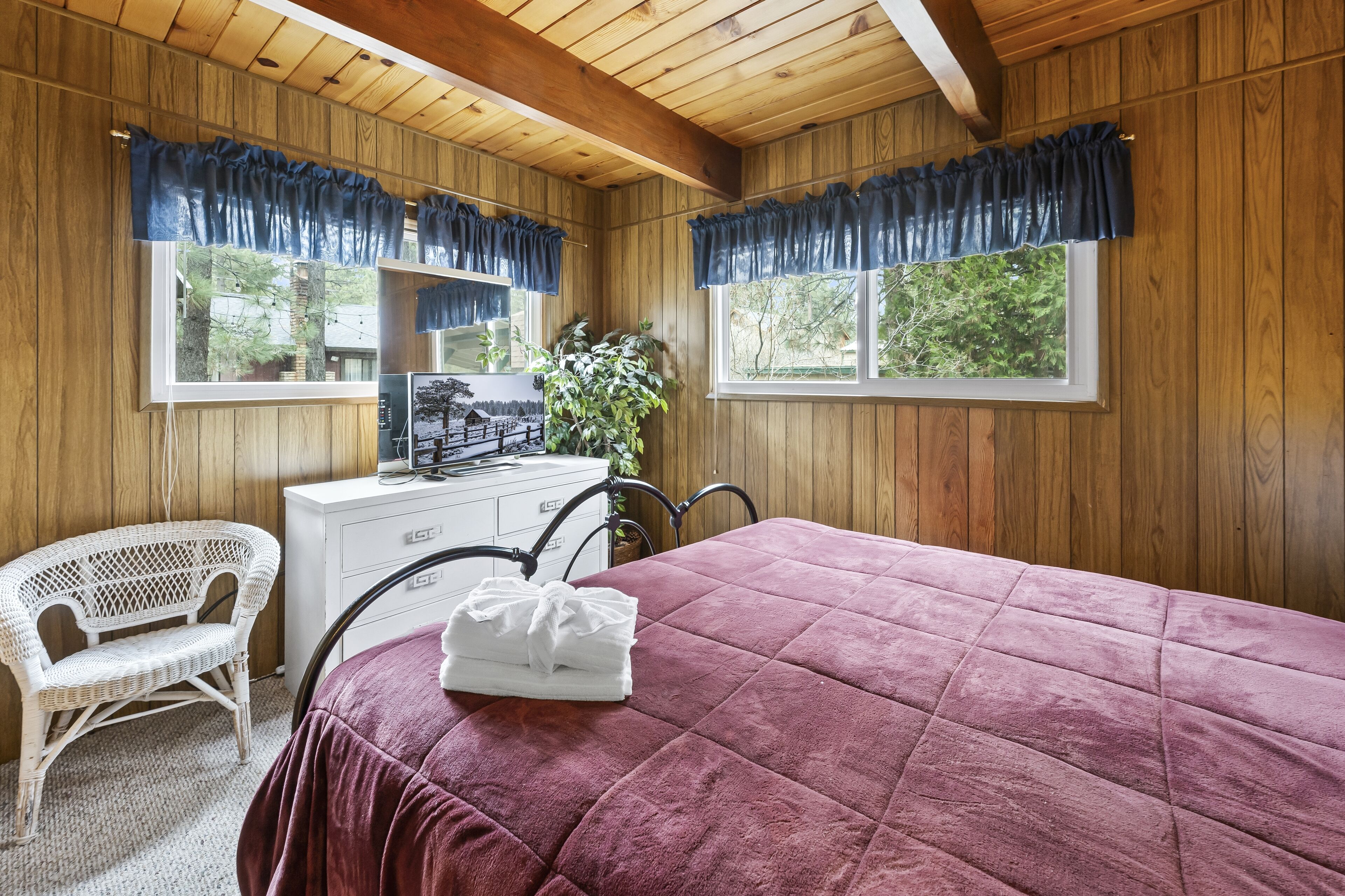 A wooden-paneled room with a bed, a desk, a chair, and a window with curtains.