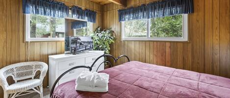 A wooden-paneled room with a bed, a desk, a chair, and a window with curtains.