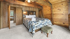Een slaapkamer in een houten chalet met een bed, een bankje en een deur naar een andere kamer.