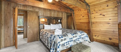 A wooden cabin bedroom with a bed, bench, and a door leading to another room.