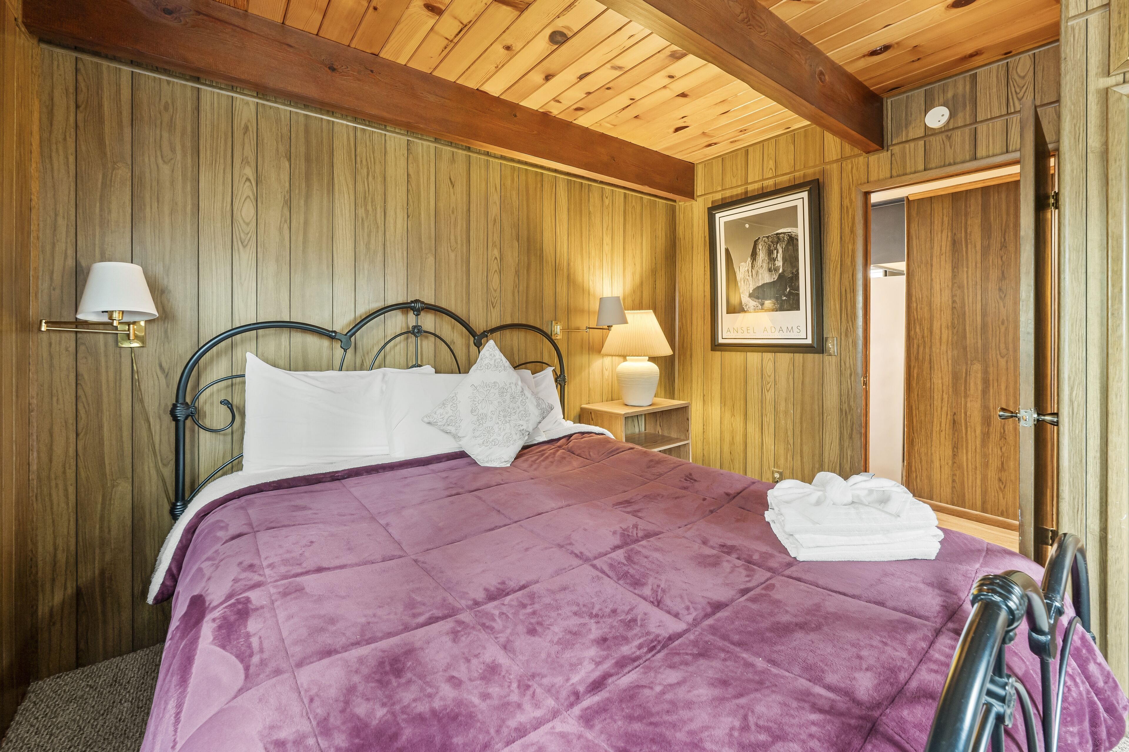 A room with a bed, wooden walls, a framed picture, and a door.