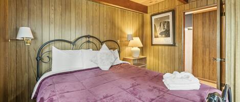 A room with a bed, wooden walls, a framed picture, and a door.