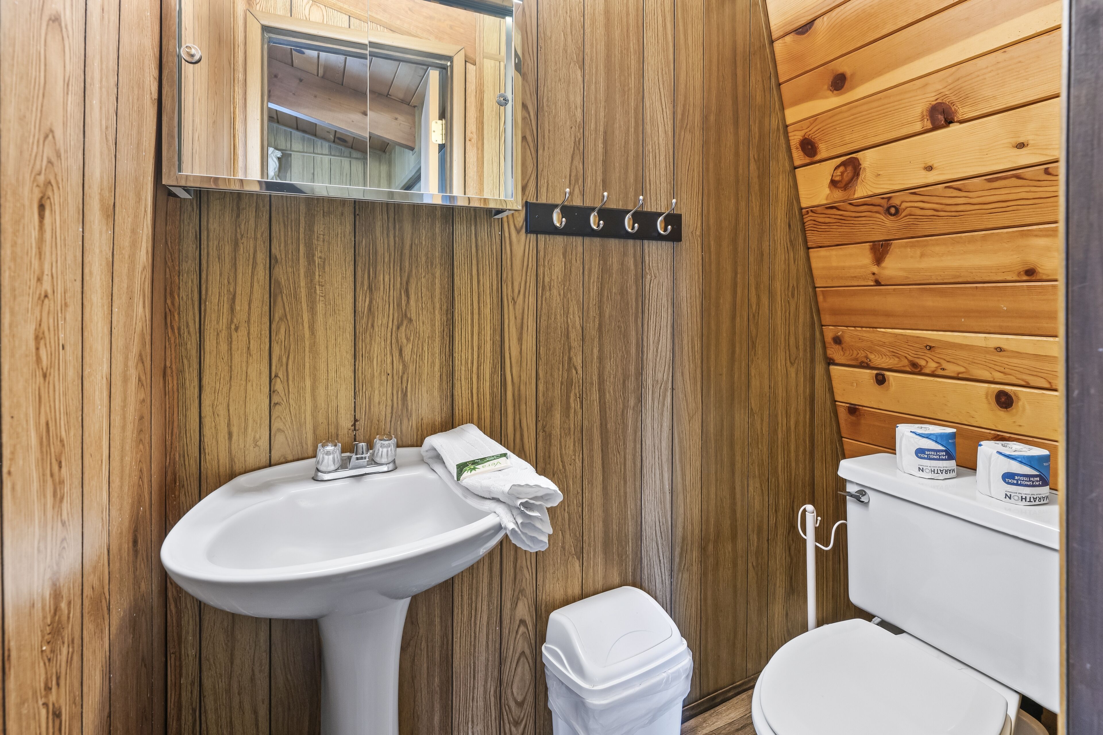 A wooden-paneled bathroom with a white sink, mirror, and toilet.