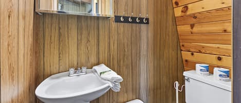 A wooden-paneled bathroom with a white sink, mirror, and toilet.